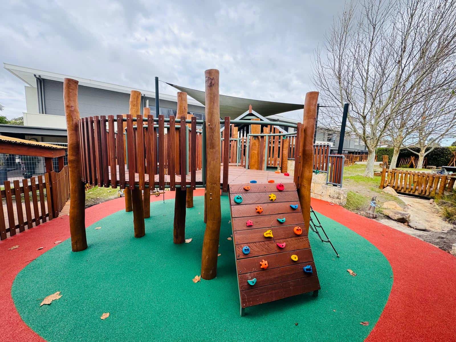 about Colorful outdoor children’s play structure with climbing wall, slide, and safety surface, ideal for preschool or daycare play areas. Durable wooden construction and vibrant safety mats enhance fun and safety.
