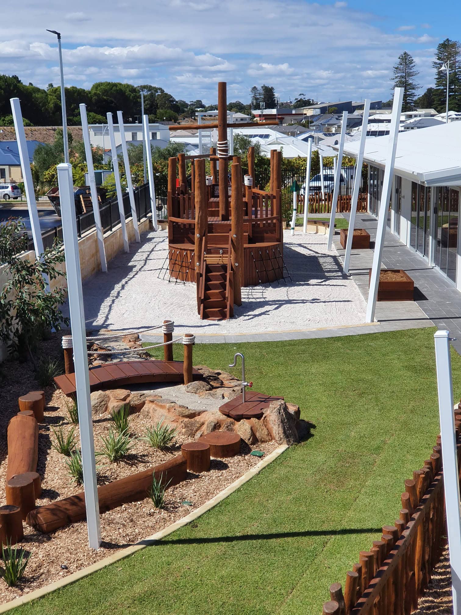 Vibrant outdoor children's playground with wooden climbing structures, sandpit, and lush green grass, perfect for kids' recreation and outdoor activities at DG Play.