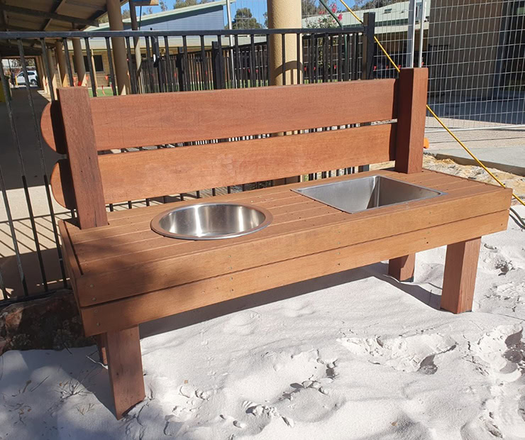 Bench with integrated stainless steel sink and bowl, outdoor playground, durable wooden seating area for children, sand and playground safety features, ideal for recreational spaces and park amenities.