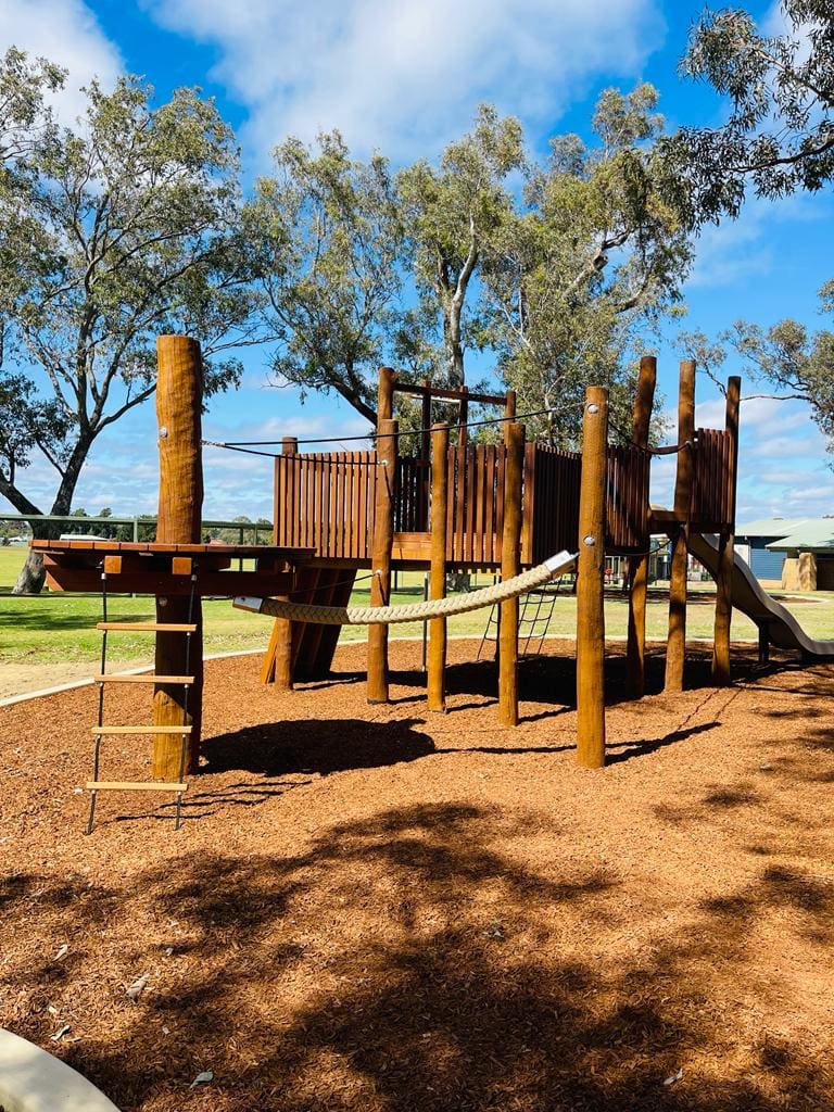 Adventure playground with wooden structures and climbing ropes, set in a sunny outdoor park with trees and open spaces, perfect for children's outdoor activities and playtime.