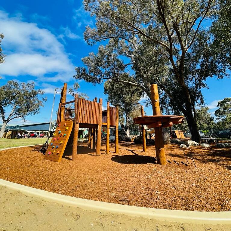 Playground structure at Big John Fort in DG Play, featuring climbing walls and a wooden tower for children’s outdoor fun.