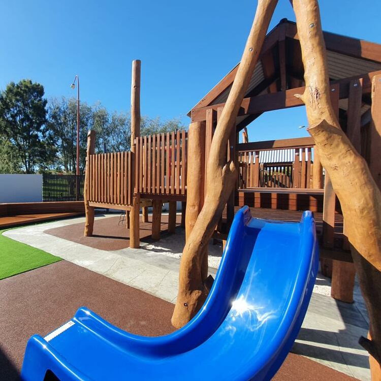 Outdoor playground with wooden playhouse and vibrant blue slide for children’s fun and recreation. Perfect for parks, schools, and family entertainment areas.