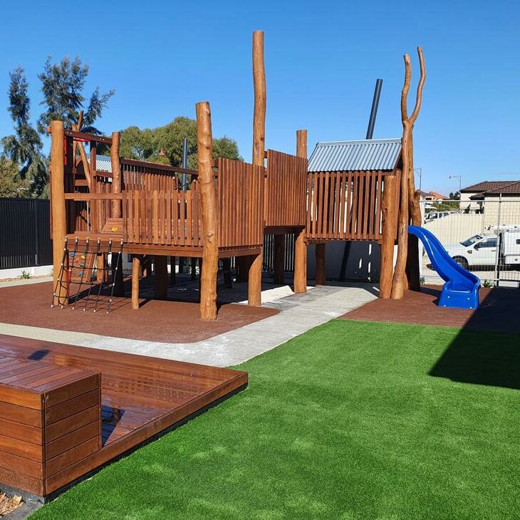 Playground with natural timber play equipment and a small blue slide for children.