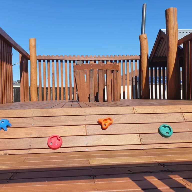 Wooden outdoor climbing wall with colorful handholds on a sunny day, perfect for children's play area or backyard entertainment.