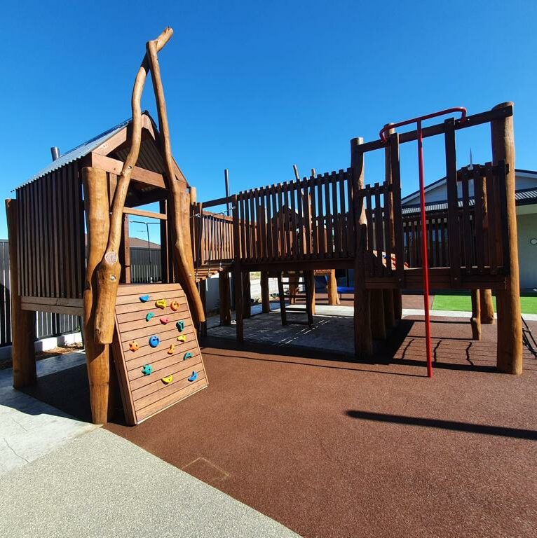Wooden playground structure with climbing wall and slides at DG Play, outdoor kids' play area, safe and fun recreational space, ideal for children’s entertainment and physical activity.